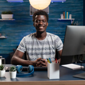 portrait-smiling-man-person-looking-into-camera-while-working-remote-from-home-business-project-typing-financial-course-computer-businessman-sitting-desk-table-living-room-office